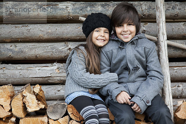 Mädchen und Junge auf Holzstapel sitzend  lächelnd  Portrait