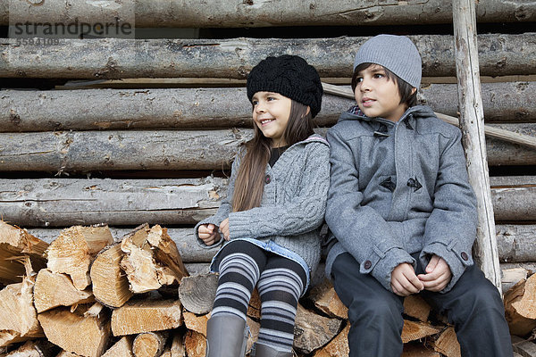 Mädchen und Junge sitzen auf einem Holzstapel