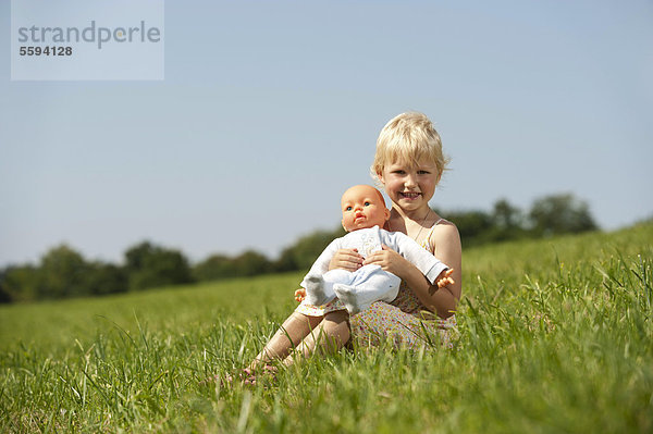 Mädchen mit Babypuppe im Gras  lächelnd  Portrait