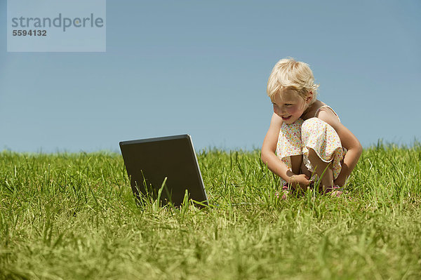 Mädchen mit Laptop im Gras sitzend