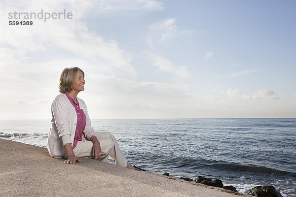 Spanien  Mallorca  Seniorin am Meer sitzend  lächelnd