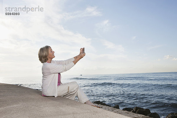 Spanien  Mallorca  Seniorin sitzend und telefonierend am Meer  lächelnd