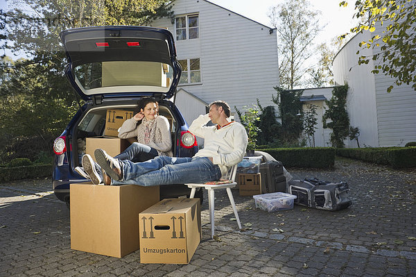 Deutschland  Bayern  Grobenzell  Paar entspannt auf Stuhl neben dem Auto  lächelnd