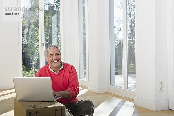 Senior Mann mit Laptop auf Karton  lächelnd