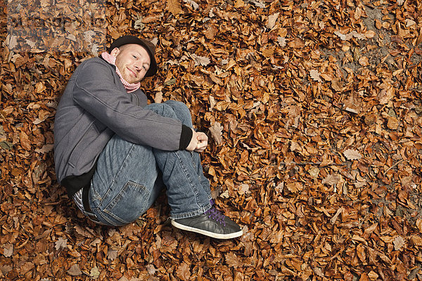 Junger Mann im Laub liegend  lächelnd  Portrait
