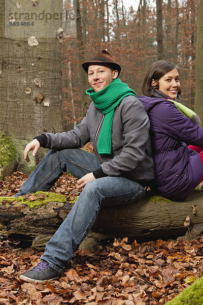 Deutschland  Berlin  Wandlitz  Paar auf Baumstamm sitzend  lächelnd  Portrait