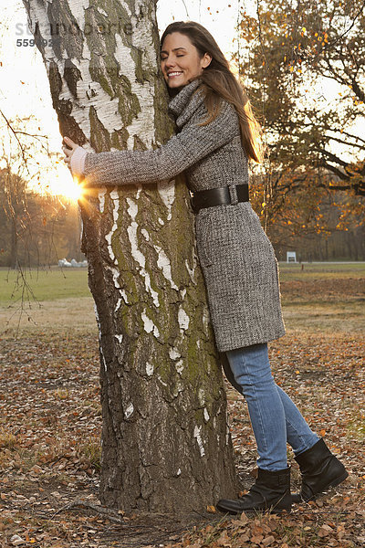 Mittlere erwachsene Frau umarmt Baum  lächelnd