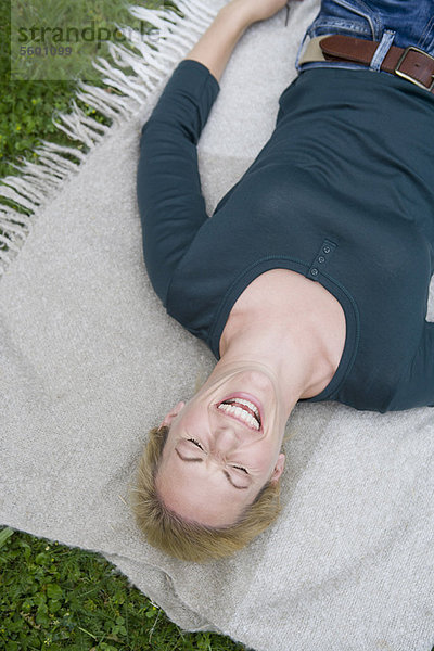 Frau lacht auf Decke im Gras