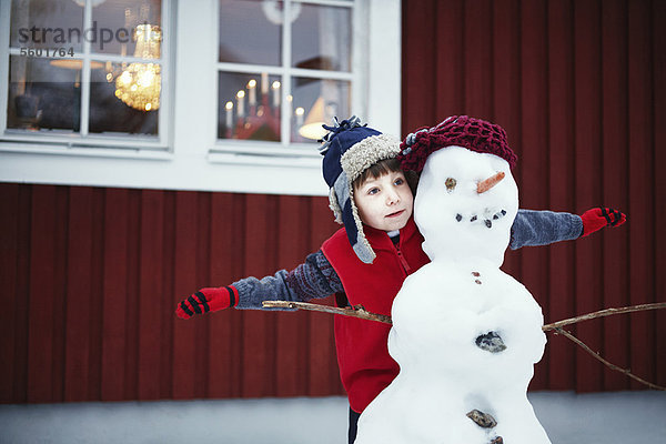 Junge spielt mit Schneemann im Freien