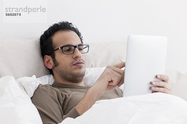Mann mit Tablet-Computer im Bett