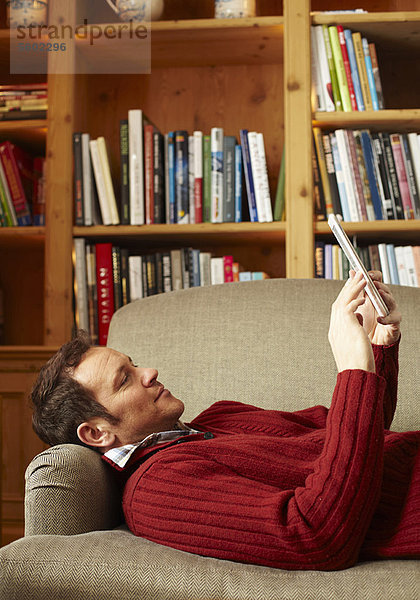 Mann liest Buch auf Sofa