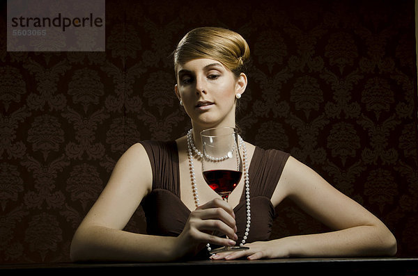 Junge Frau mit Perlenkette und Perlenohring  mit Rotwein im Rotweinglas