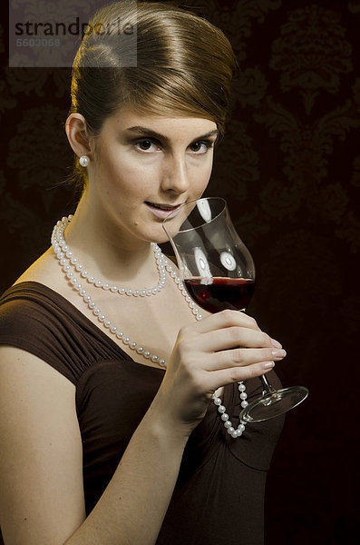 Junge Frau mit Perlenkette und Perlenohring  trinkt Rotwein aus Rotweinglas