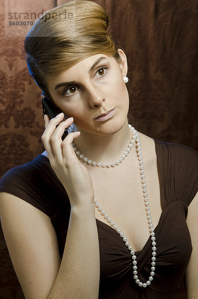 Junge Frau mit Perlenkette und Perlenohring  telefoniert mit Handy