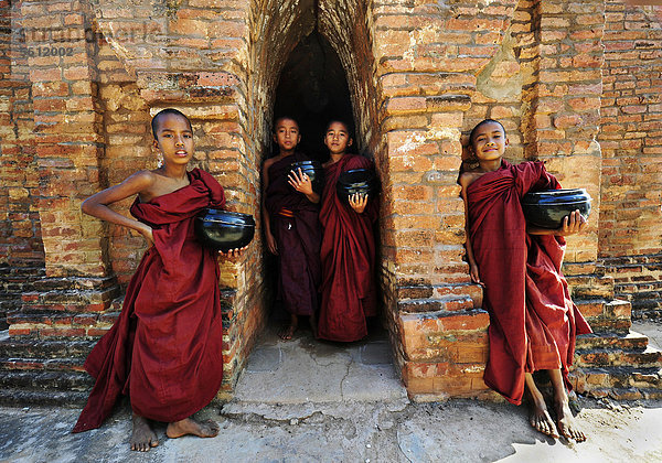 Junge buddhistische Novizen mit Almosenschalen vor alten Klostermauern bei der Shwezigon Pagode in Bagan  Myanmar  Birma  Südostasien  Asien