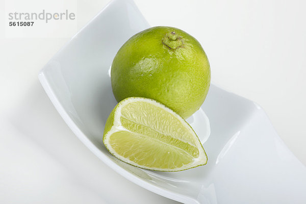 Limetten (Citrus latifolia)  ganz und geschnitten  in einer weißen Schale