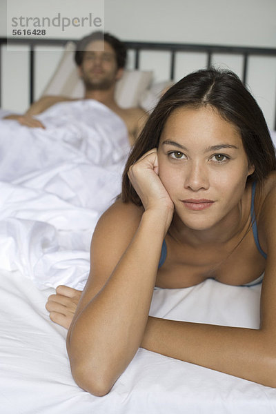 Junge Frau auf dem Bett liegend  Freund im Hintergrund