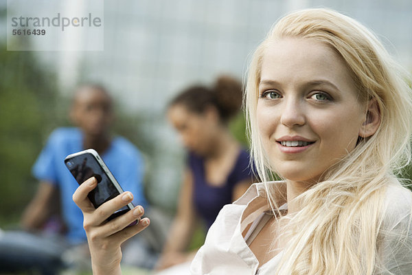 Junge Frau mit Handy  Menschen im Hintergrund  Portrait