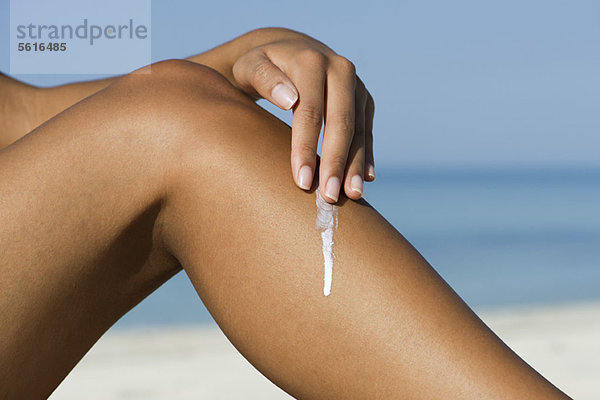 Frau  die Sonnencreme auf das Bein am Strand aufträgt  abgeschnitten