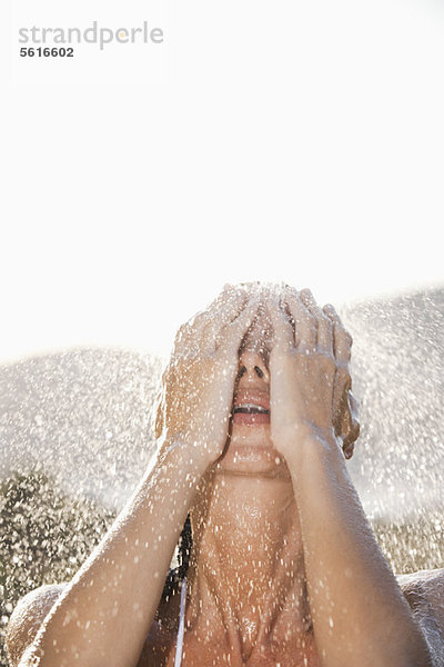 Frau wäscht Gesicht unter der Dusche im Freien