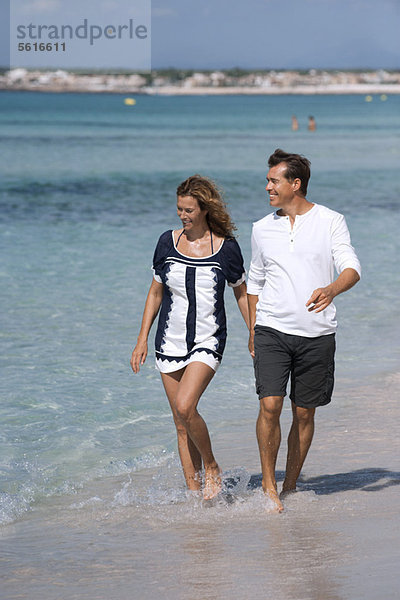 Paar  das am Strand spazieren geht und Hände und Knöchel tief im Wasser hält.