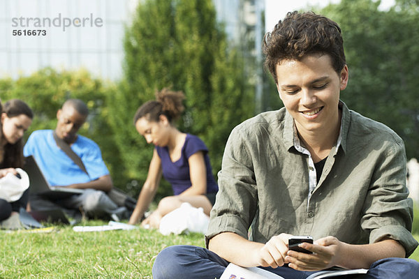 Junger Mann SMS mit Handy  Gruppe von Menschen im Hintergrund
