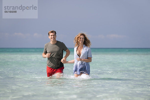 Paar steht knietief im Wasser und hält sich an den Händen.