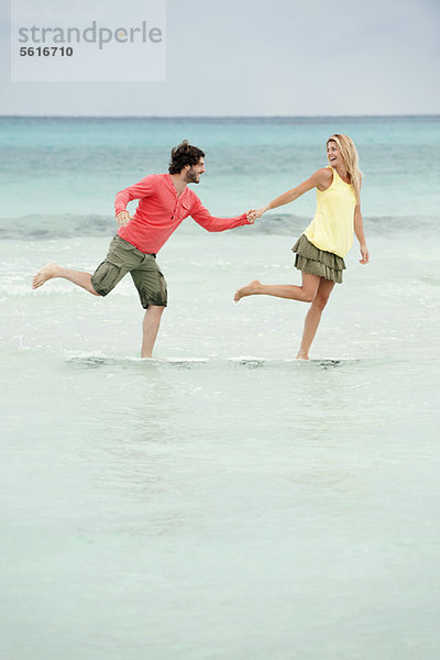 Paar steht auf einem Bein im Wasser am Strand  hält sich an den Händen