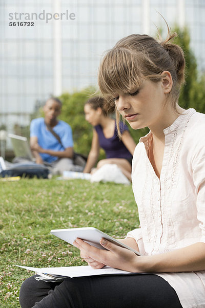 Junge Frau liest elektronisches Buch auf Gras  Menschen im Hintergrund