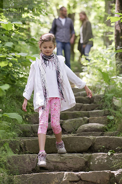 Mädchen geht im Wald die Steintreppe hinunter  Eltern im Hintergrund