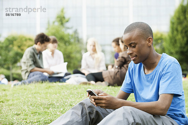 Junger Mann SMS mit Handy  Leute im Hintergrund