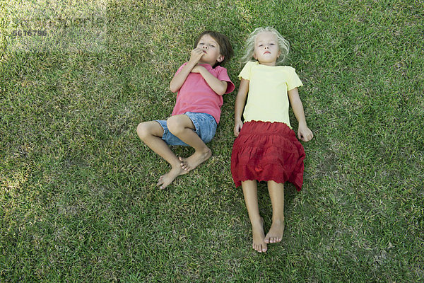 Kinder liegen zusammen auf Gras und schauen in die Kamera.