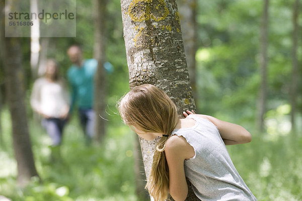 Mädchen beim Wandern hinter Bäumen im Wald