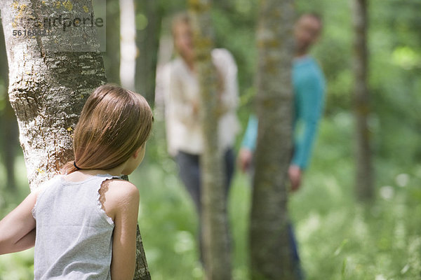 Mädchen beim Verstecken mit Eltern im Wald  Rückansicht