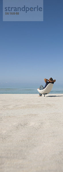 Mann entspannt im Stuhl am Strand  Rückansicht