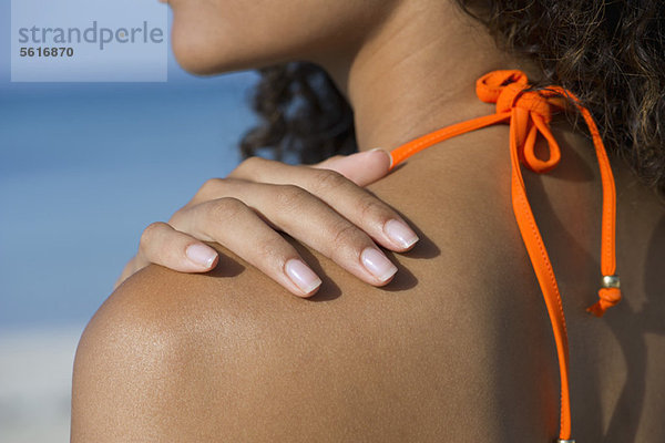 Frau berührt nackte Schulter am Strand  abgeschnitten