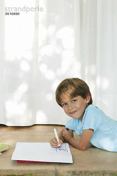 Junge auf dem Boden liegend  Zeichnung im Notizbuch
