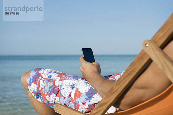 Mann mit Handy am Strand sitzend  abgeschnitten