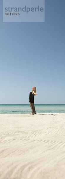 Frau am Strand stehend mit ausgestreckten Armen  Seitenansicht