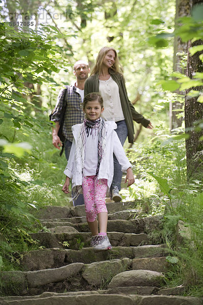 Mädchen geht im Wald die Steintreppe hinunter  Eltern im Hintergrund