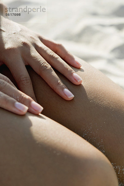 Frau berührt nackte Beine am Strand  abgeschnitten