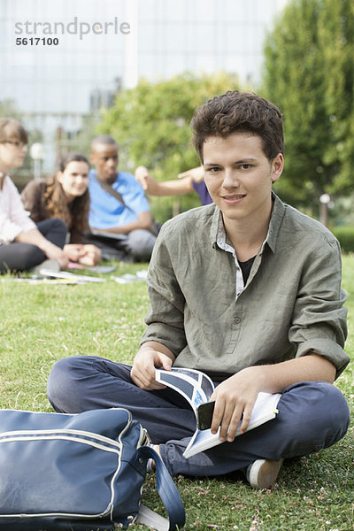 Junger Mann auf Gras sitzend  Menschen im Hintergrund  Portrait