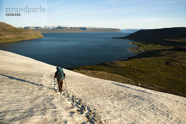 Wanderin durchquert das Schneefeld  Blick auf Ort Hesteyri  Fjord Hesteyrarfjör_ur  Hesteyrarfjördur  Hornstrandir  Westfjorde  Island  Europa