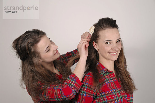 Zwillingsschwestern  die eine steckt der anderen eine Haarspange mit einer Rose in die Haare