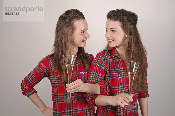 Zwillingsschwestern mit Sektgläsern trinken Brüderschaft