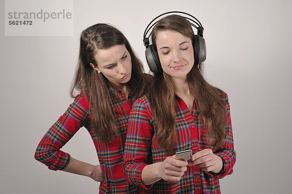 Zwillingsschwestern  die eine mit iPod und Kopfhörern  die andere schaut neidisch
