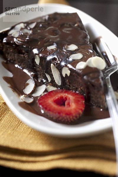 Ein Stück Schokoladenkuchen mit Schokosauce  Mandelblättchen und Erdbeere