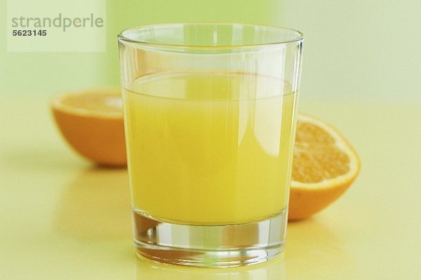 Ein Glas Orangensaft vor Orangenhälften