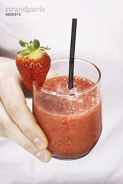 Hand hält ein Glas Erdbeer-Smoothie