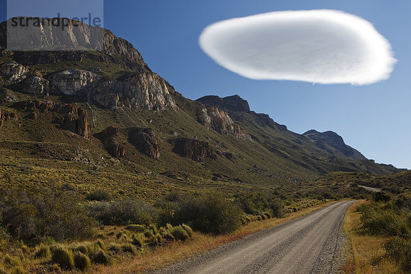 Sandpiste nach Cochrane im Abendlicht unter einer großen weißen Kumulus-Wolke  Altocumulus lenticularis  Rio Chacabuco  Cochrane  Region de Aysen  Patagonien  Chile  Südamerika  Amerika